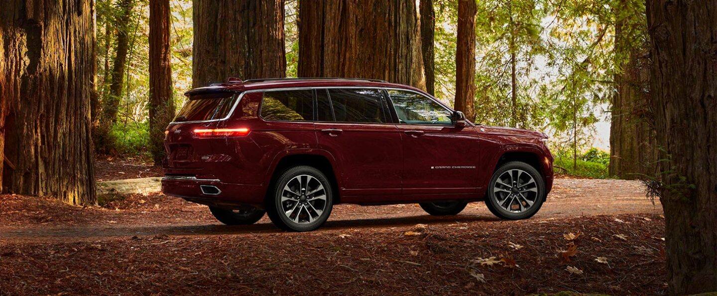 A three-quarter profile view of a 2021 Jeep Grand Cherokee L Overland parked off-road in the woods.