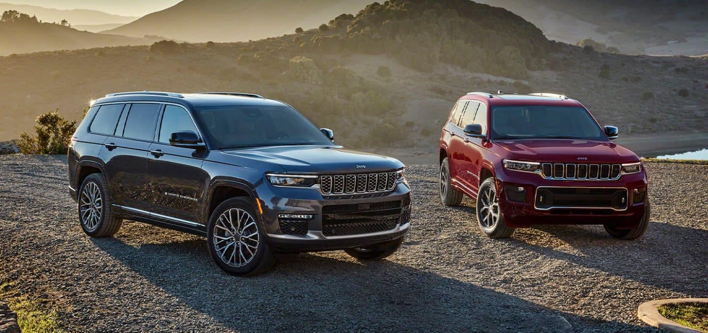 Display Two 2021 Jeep Grand Cherokee L models–a Summit Reserve and an Overland, parked on sandy terrain in the mountains.