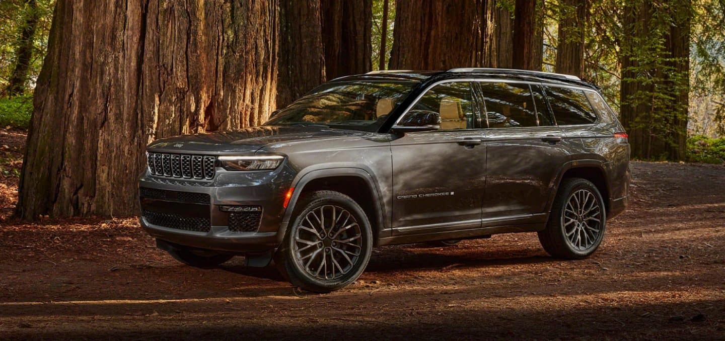 Display A three-quarter profile view of a 2021 Jeep Grand Cherokee L Summit Reserve parked in the woods, next to several large trees.