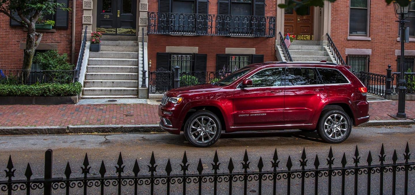 Display The 2021 Jeep Grand Cherokee Summit parked on a street outside a row of townhouses.