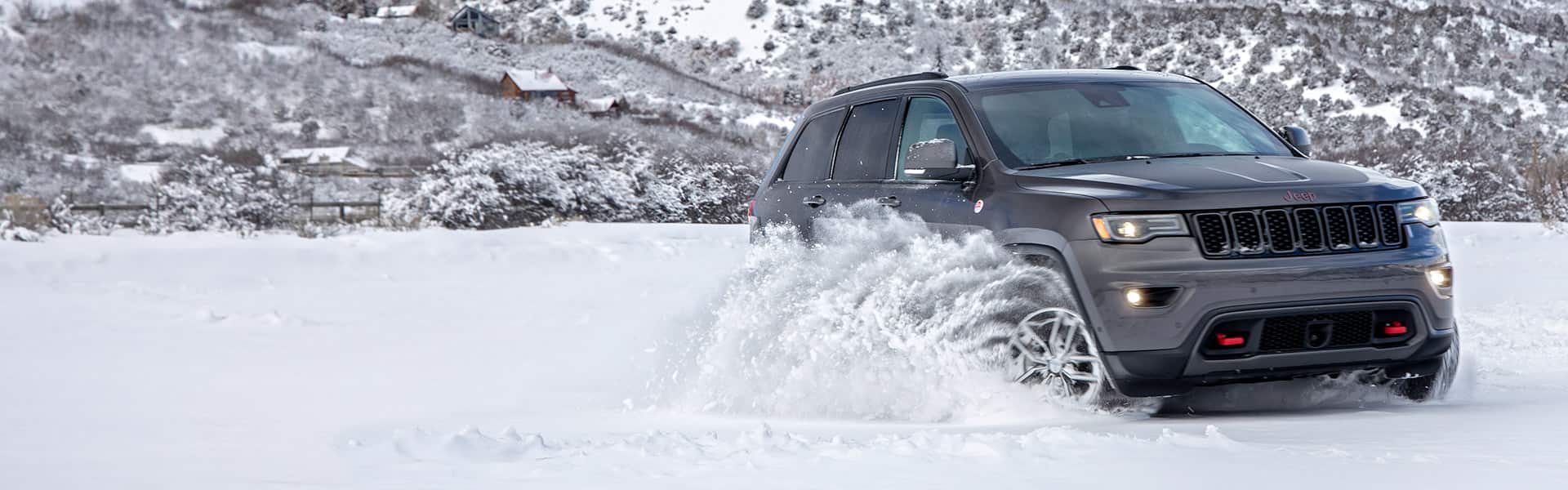 2021 Jeep Grand Cherokee Trailhawk being driven off-road in winter, with sprays of snow obscuring its wheels.