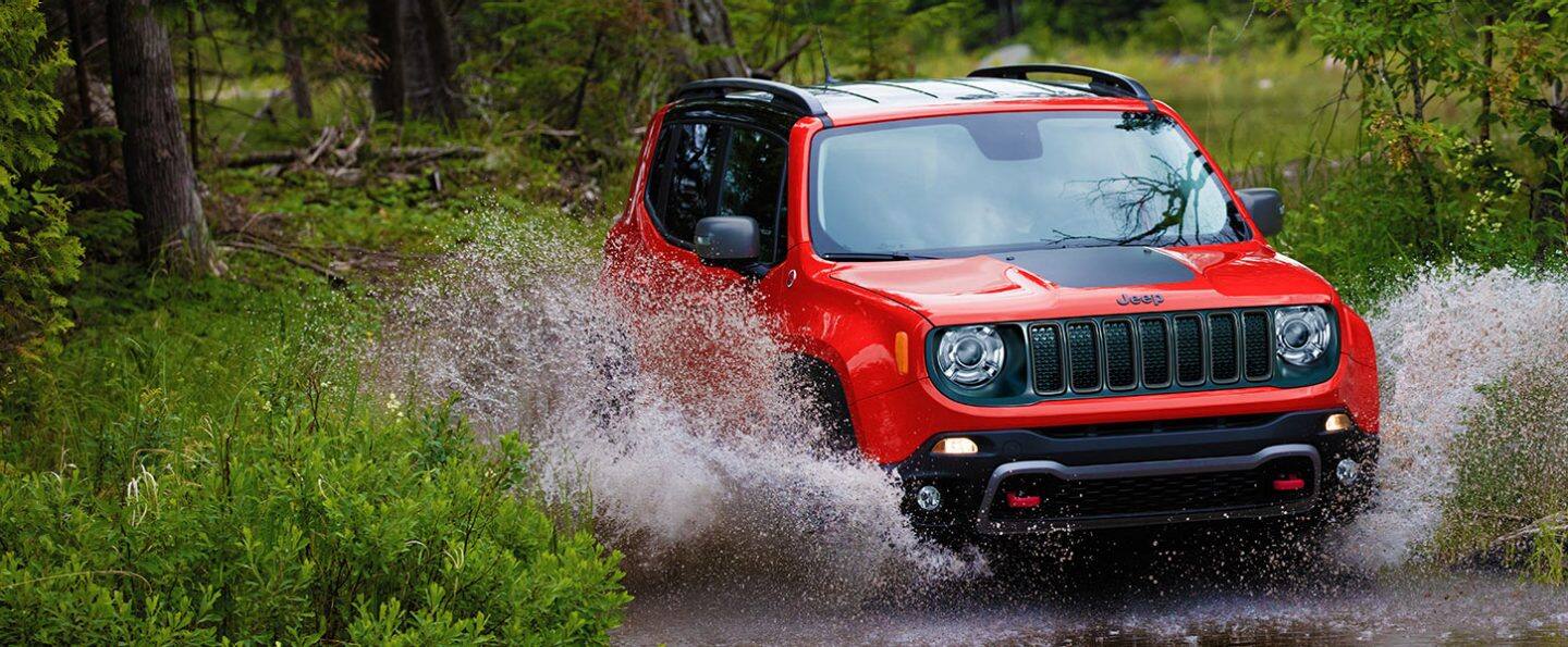 Un Jeep Renegade 2021 rojo salpicando agua mientras vadea por un arroyo.