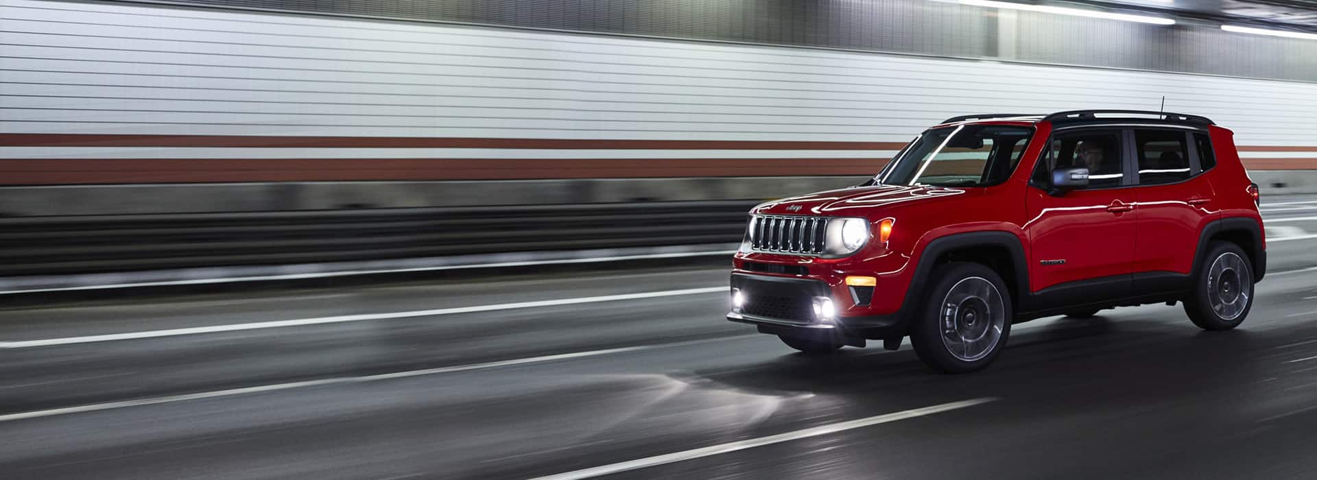 A red 2021 Jeep Renegade being driven through a tunnel with headlamps lit.