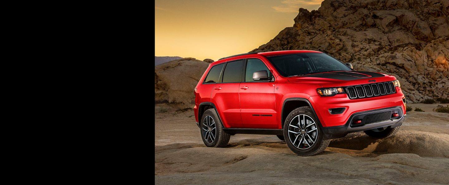 The 2021 Jeep Grand Cherokee Trailhawk parked on uneven desert terrain with one wheel elevated on a rock.
