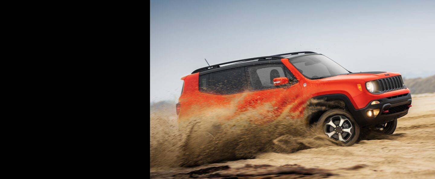 The 2021 Jeep Renegade Trailhawk being driven off-road on sandy terrain with a dust cloud rising from its wheels.