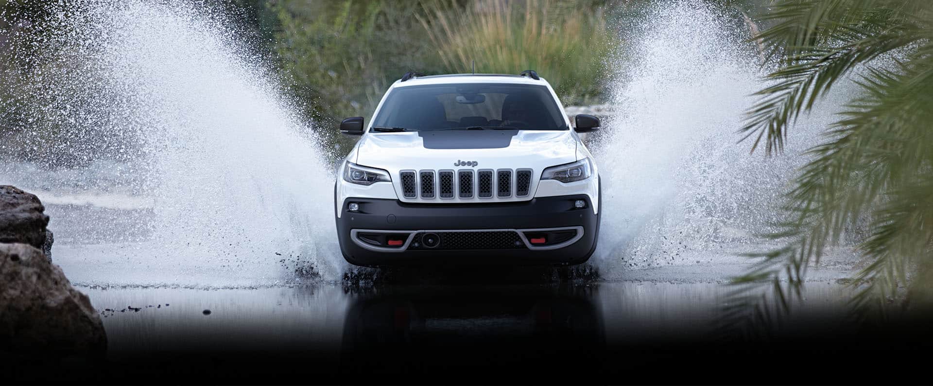 A head-on view of the 2022 Jeep Cherokee Trailhawk being driven through a stream with sprays of water on both sides.