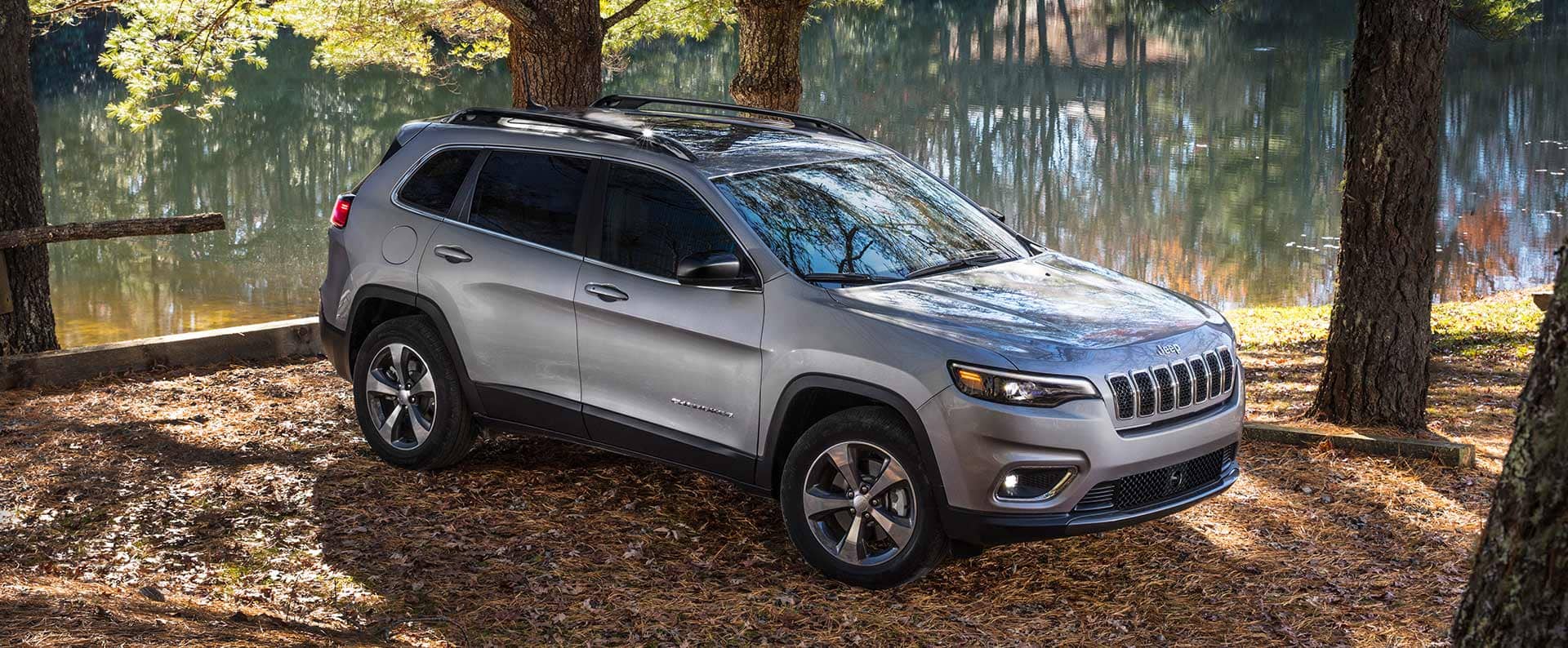 A three-quarter front profile of the 2022 Jeep Cherokee Limited, parked in a wooded area by the water.