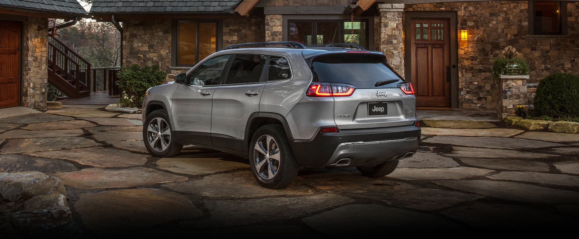 A three-quarter rear view of the 2022 Jeep Cherokee Limited, parked on a stone-paved driveway outside a sprawling chalet.