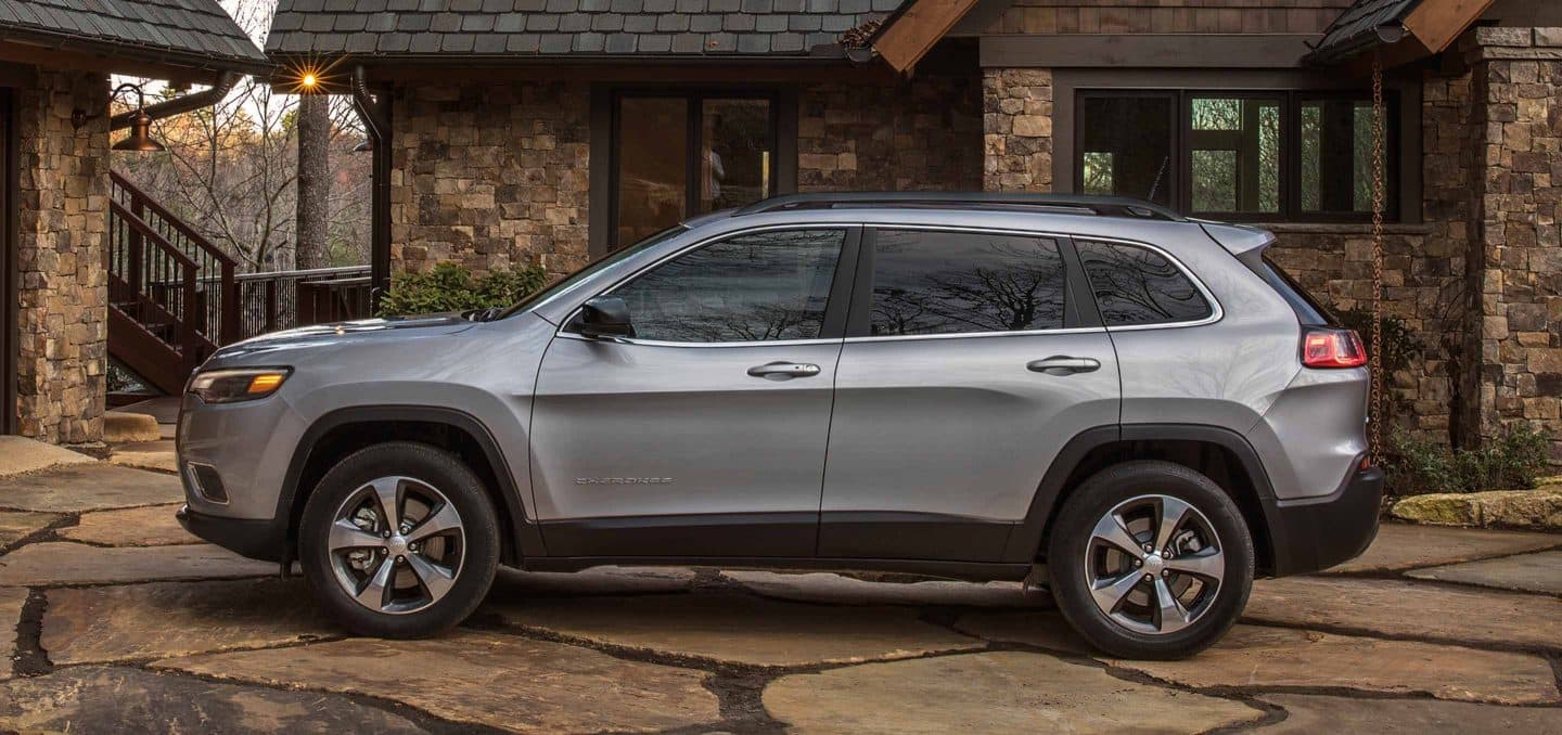 Display A side profile of the 2022 Jeep Cherokee Limited, parked in the driveway outside a large brick house.