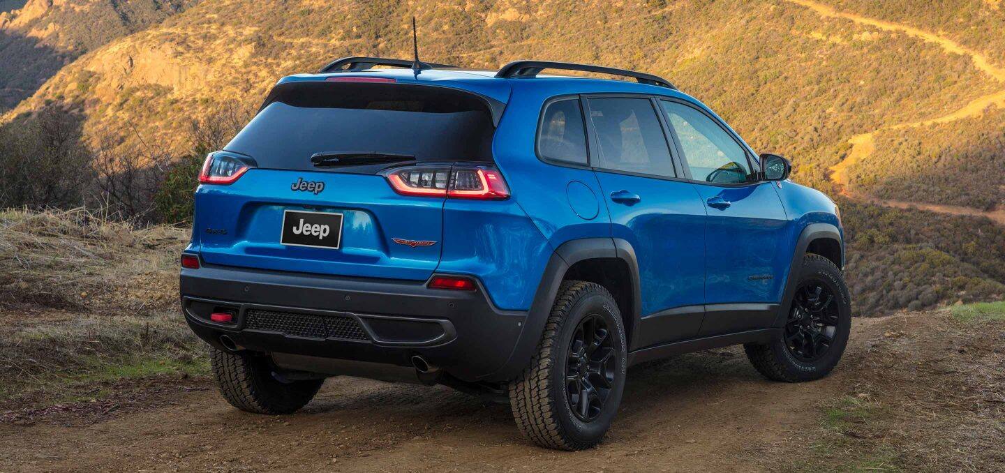 Display The 2022 Jeep Cherokee Trailhawk on a dirt track that winds ahead of it into the mountains.