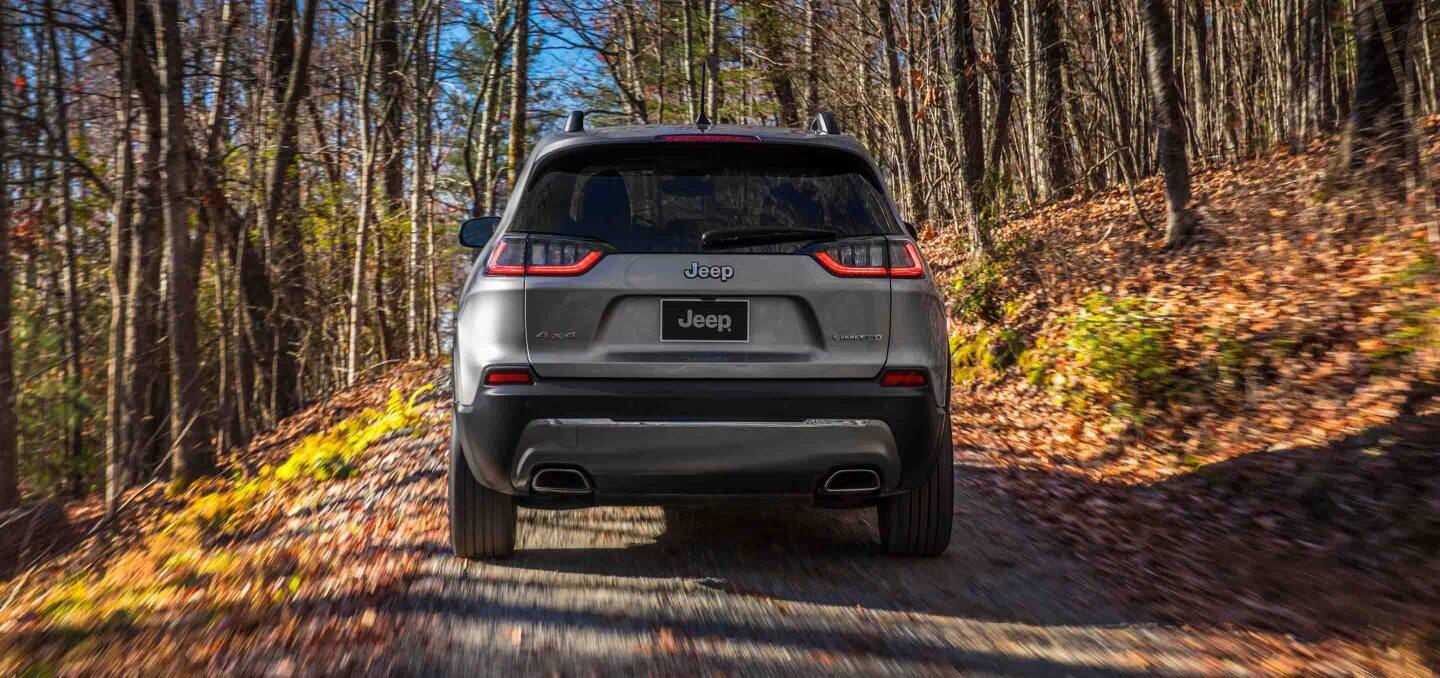 Display The 2022 Jeep Cherokee Limited being driven off-road through the woods on a clear autumn day.