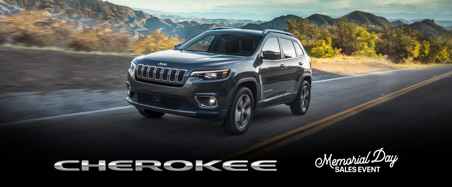 Un Jeep Cherokee Limited 2022 andando por una carretera abierta con montañas a la distancia. Logo del evento de ventas por el Día de los Caídos.