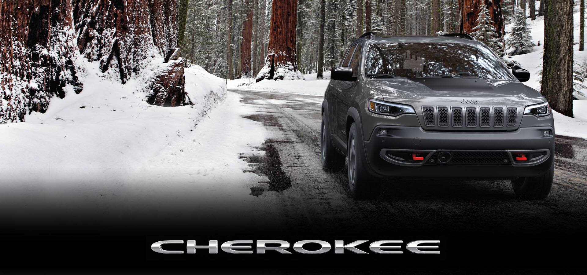 A head-on view of a 2022 Jeep Cherokee Trailhawk being driven on a snowy road through a forest. Cherokee.