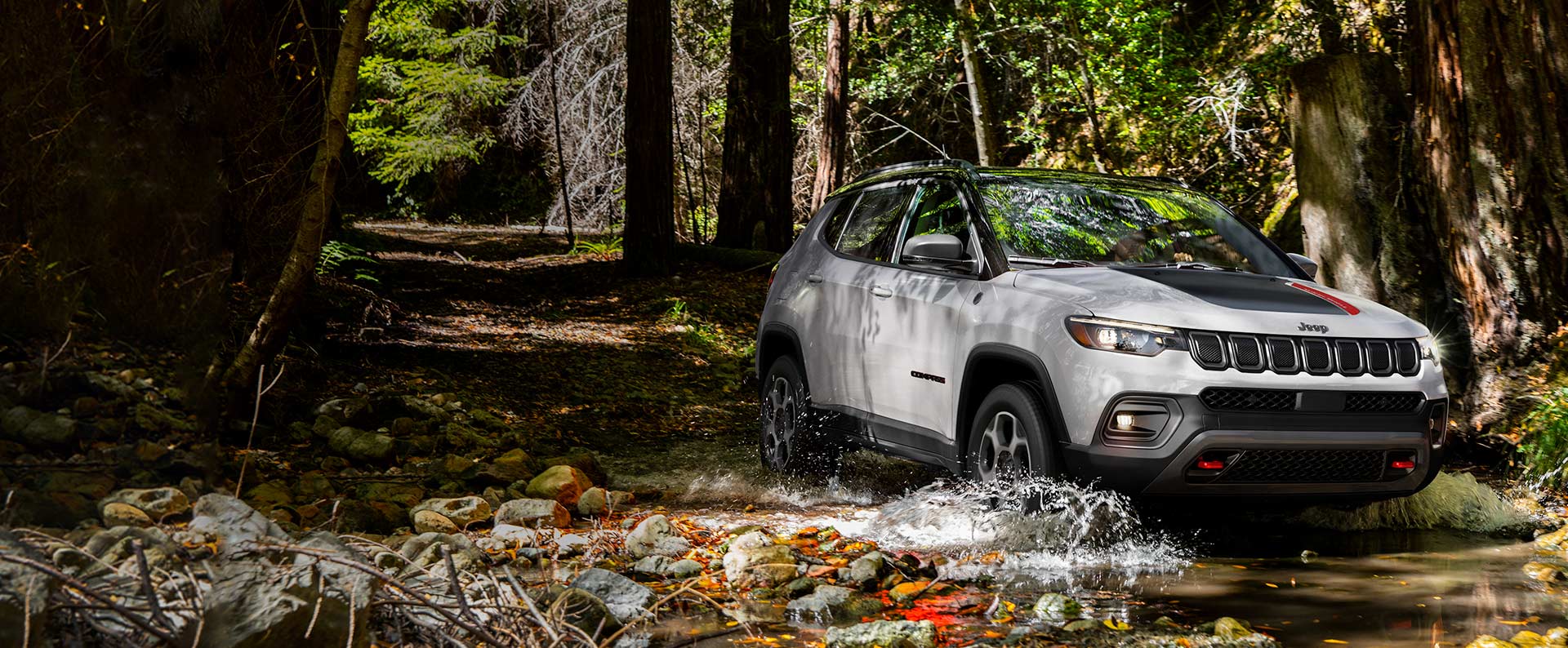 The 2022 Jeep Compass Trailhawk being driven through a stream in the woods.