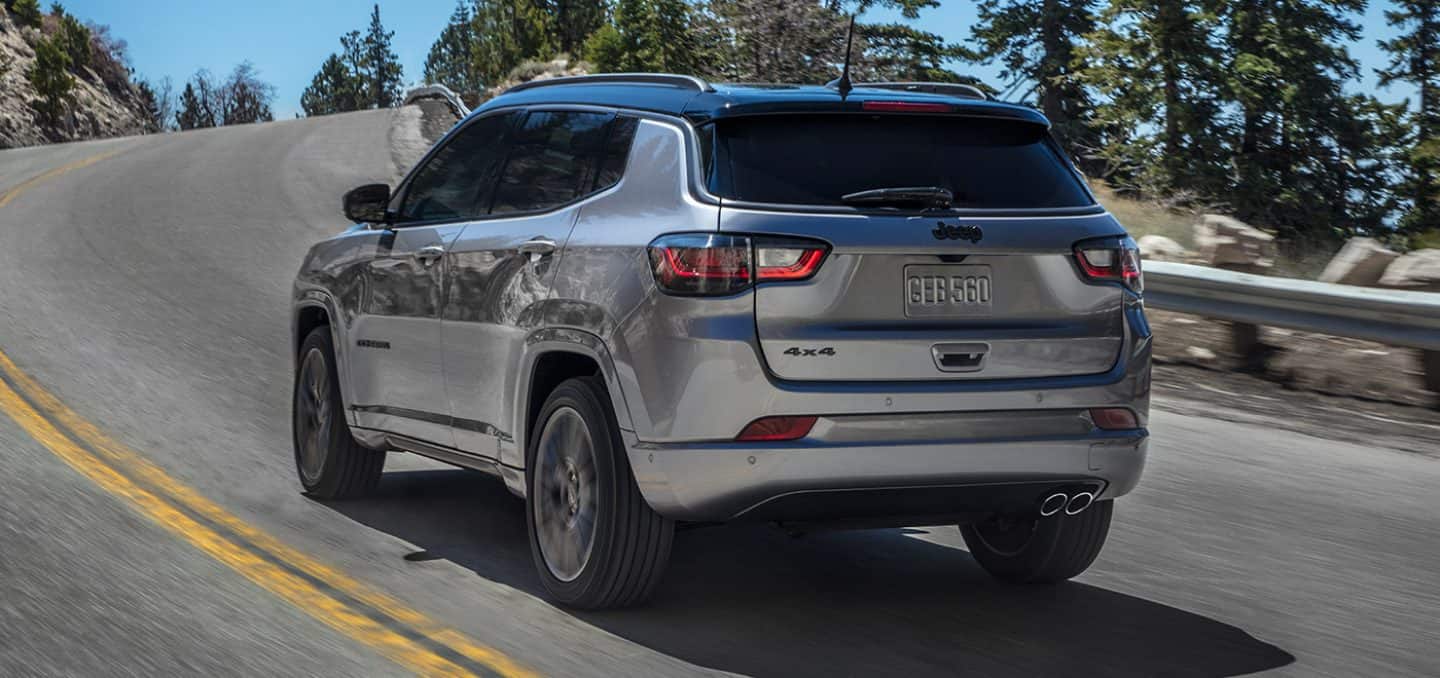 Display A three-quarter rear view of the 2022 Jeep Compass High Altitude as it rounds a curve on a mountain road.