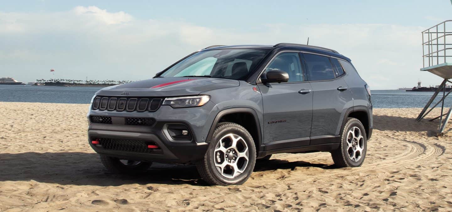 Display The 2022 Jeep Compass Trailhawk parked on a beach with tire tracks visible on the sand behind it.