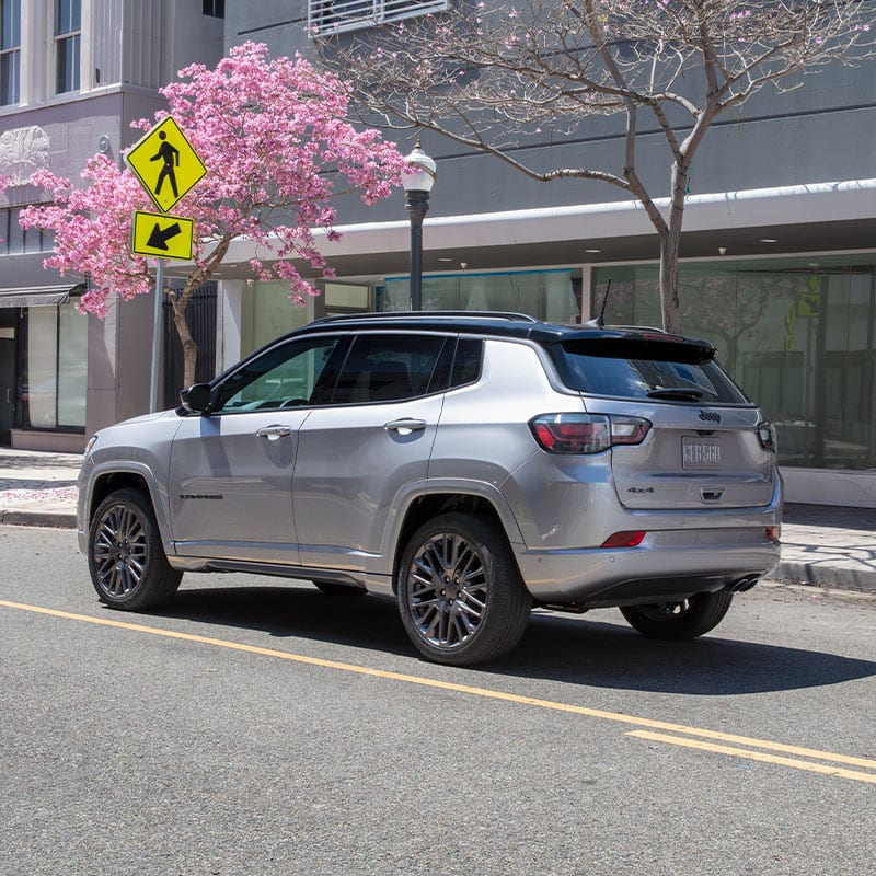 The 2022 Jeep Compass High Altitude being driven on a city street past cherry blossoms.