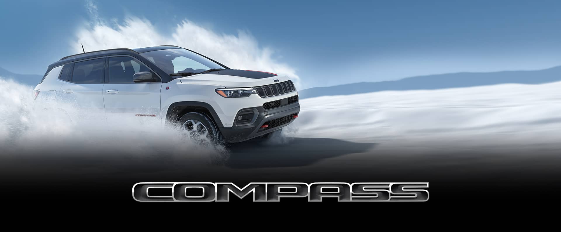 The 2022 Jeep Compass Trailhawk being driven at speed off-road in snow, with clouds of snow obscuring its wheels.