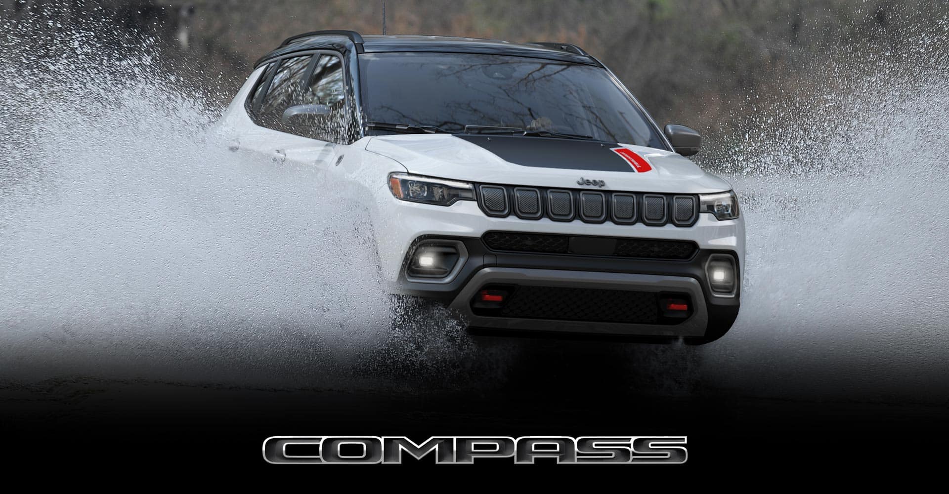 An angled front view of a white 2022 Jeep Compass Trailhawk fording a stream, spraying water up the sides of the vehicle. Compass.