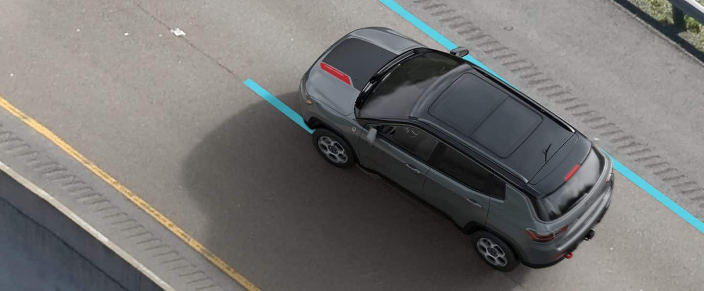 The 2022 Jeep Compass Trailhawk being driven on a road with the solid lane marking to its right and the dashed lane marking to its left highlighted in blue.