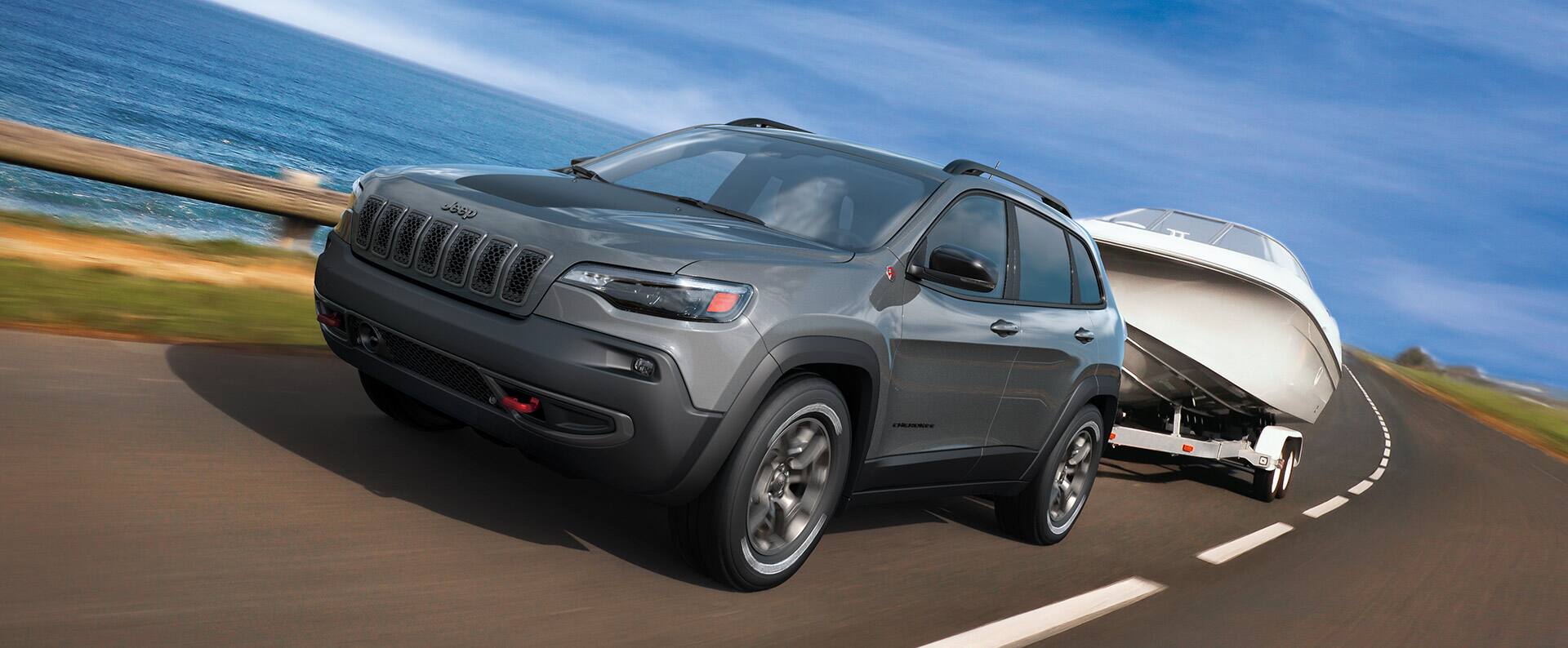 The 2022 Jeep Cherokee Trailhawk being driven beside a large body of water, towing a motorboat.