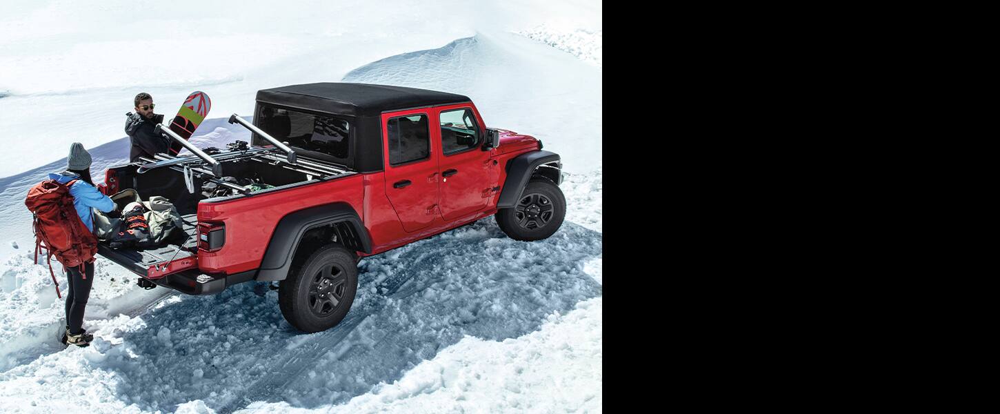 Two people unloading snowboarding gear from the bed of a 2022 Jeep Gladiator parked on snow.