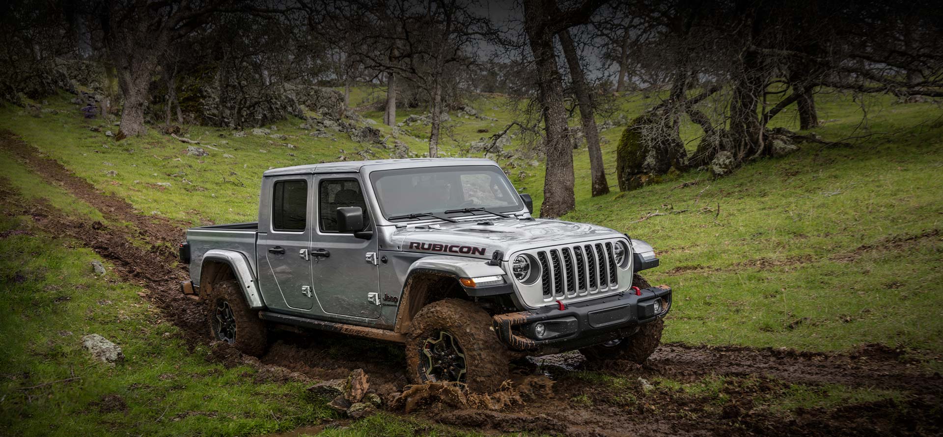 The 2022 Jeep Gladiator Rubicon being driven through a deep, muddy track on a hill.