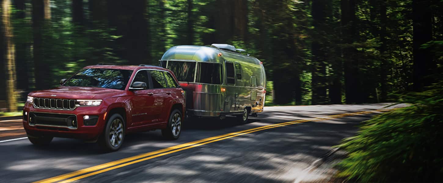 A 2022 Jeep Grand Cherokee Overland towing a travel trailer as it's driven down a forest road.