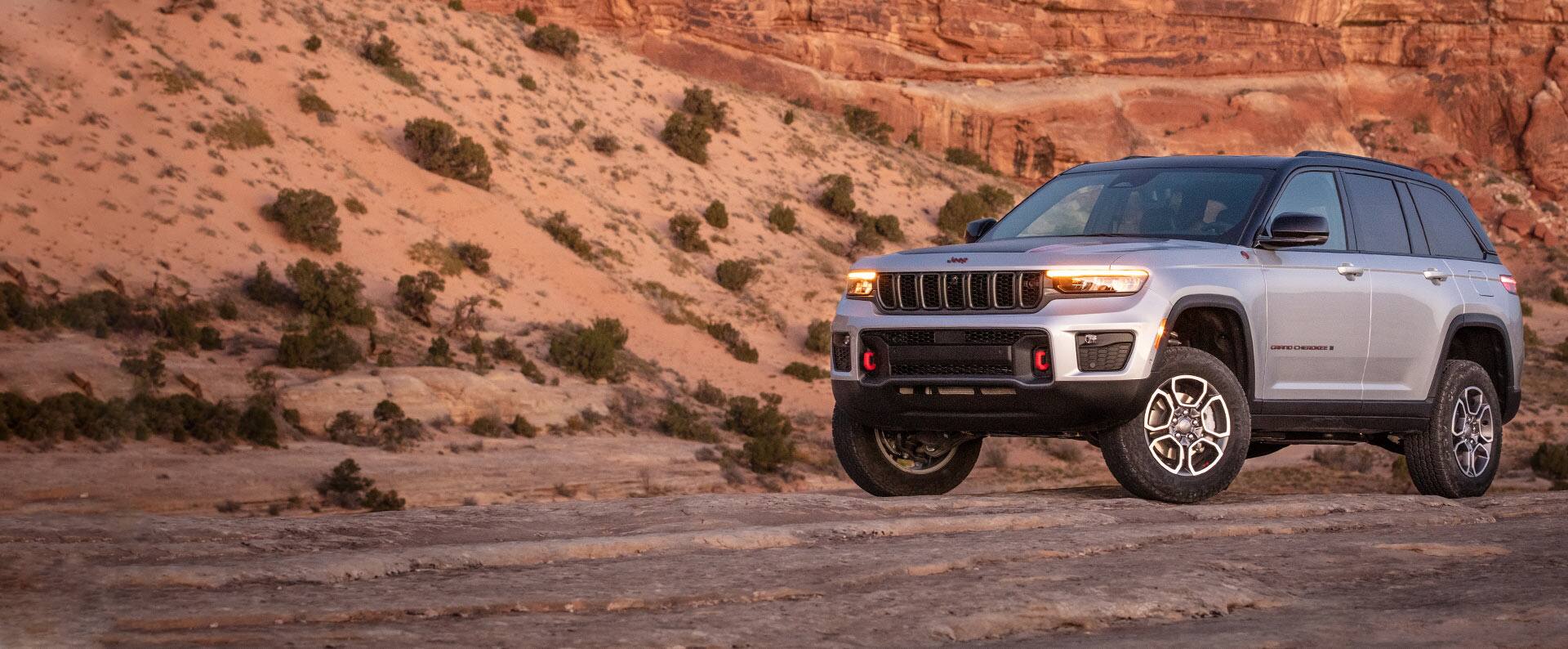 The 2022 Jeep Grand Cherokee Trailhawk parked on rocky ground that rises into a steep slope behind the vehicle.