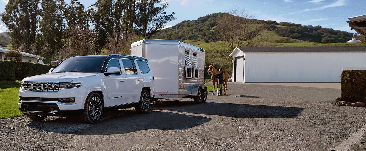 The 2022 Grand Wagoneer Series III hitched to a horse trailer with a person behind it leading a horse toward the trailer.