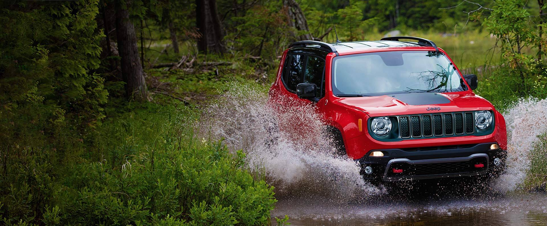 The 2022 Jeep Renegade Trailhawk being driven through a river with water splashing up on either side.