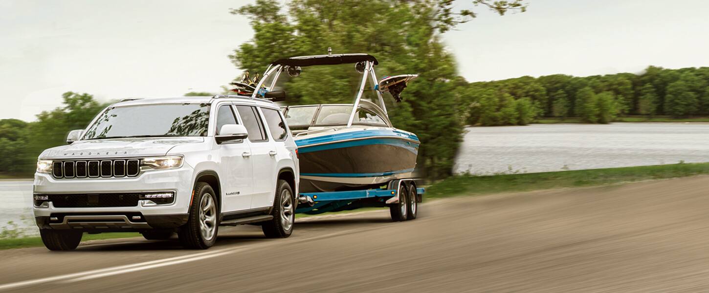 The 2022 Wagoneer Series II towing a motorboat on a paved lakeside road.
