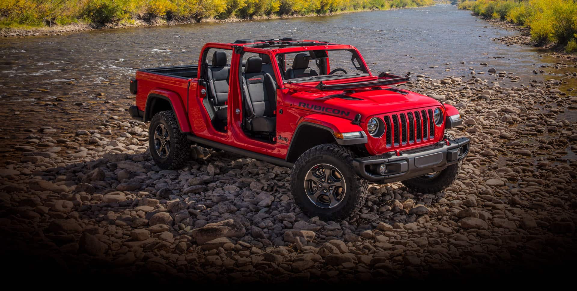 The 2022 Jeep Gladiator Rubicon with its doors off and windshield folded down, parked on a rocky beach.
