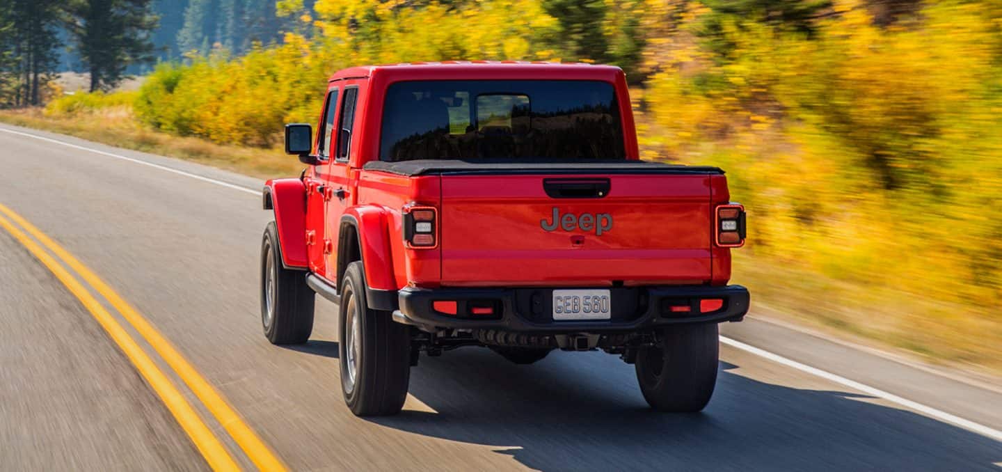 Display The 2022 Jeep Gladiator Rubicon being driven on an empty, winding road toward a range of mountains in the distance.