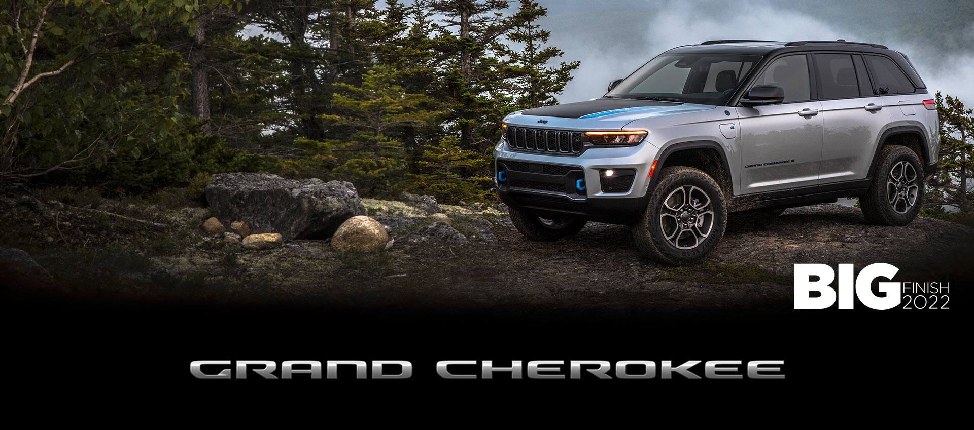 The 2022 Jeep Grand Cherokee Trailhawk 4xe parked atop a rocky clearing with evergreens nearby and misty mountains in the background. Grand Cherokee. The Big Finish 2022 logo.