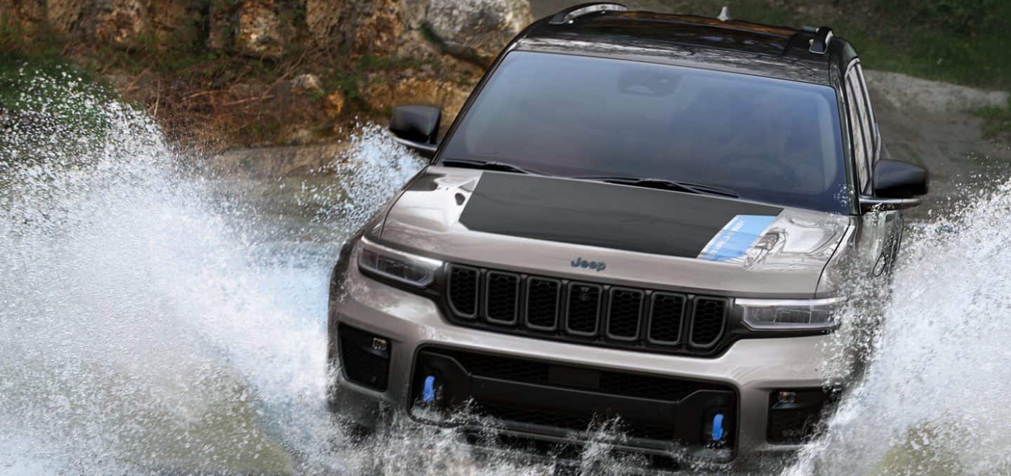 The 2022 Jeep Grand Cherokee 4xe Trailhawk splashes through water as it's driven through a river.