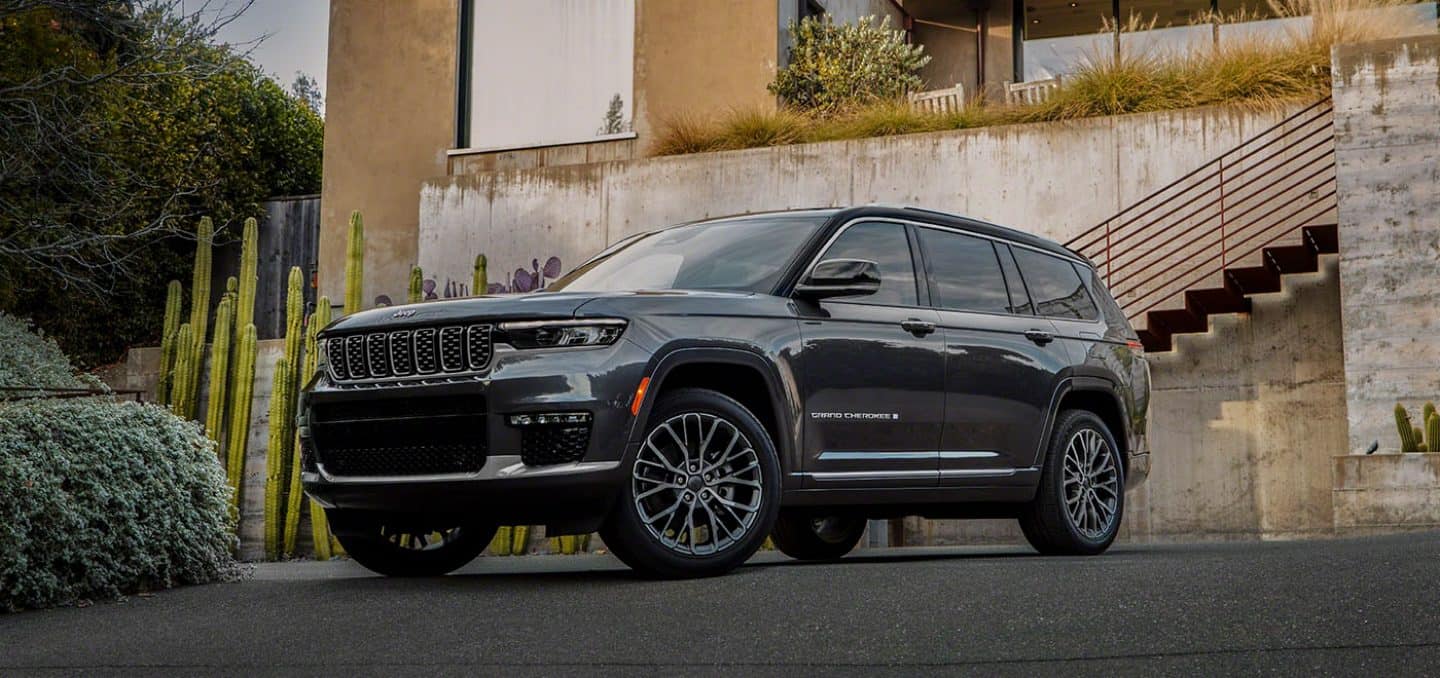 The 2022 Jeep Grand Cherokee Summit Reserve parked in front of a large, sun-drenched residence.