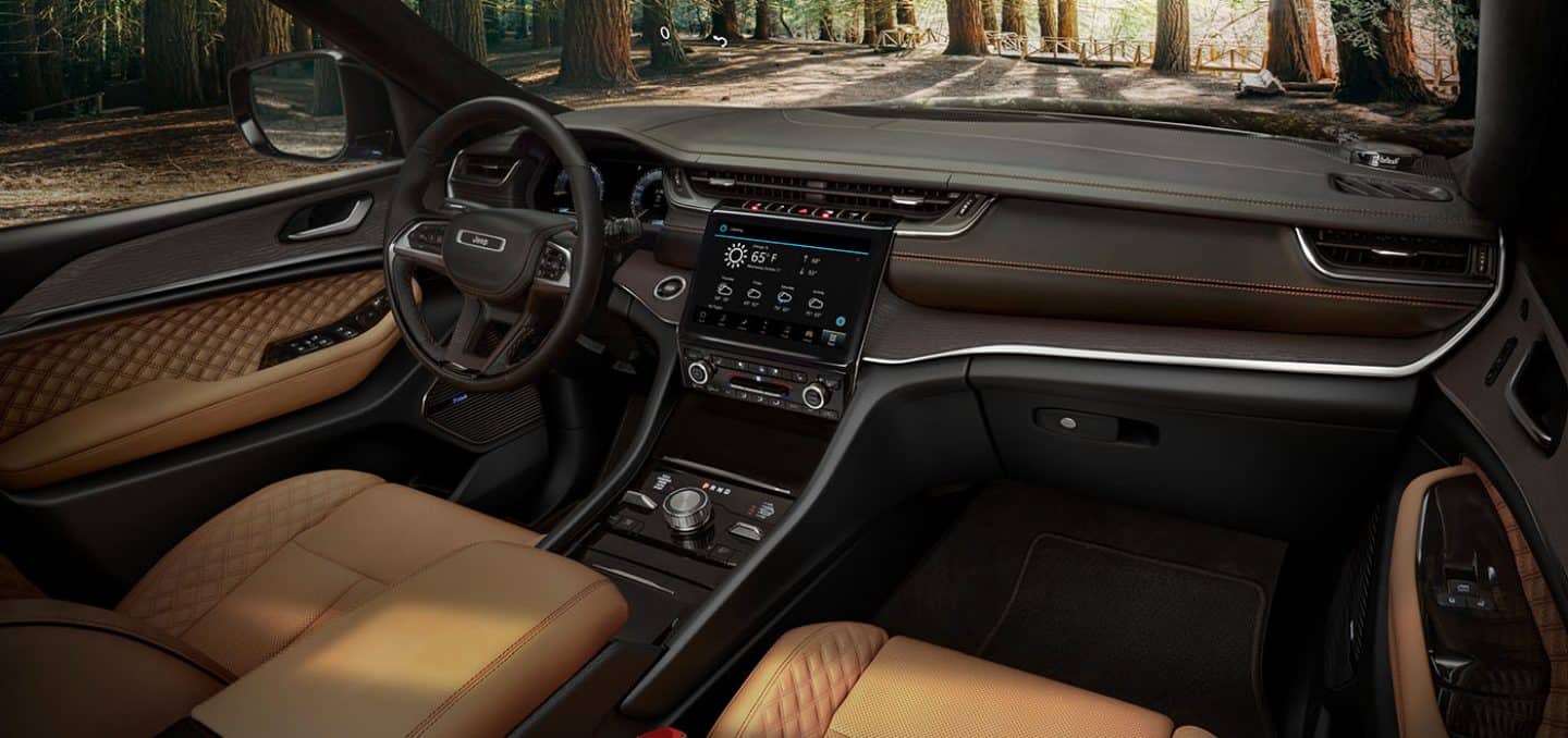 The interior of the 2022 Jeep Grand Cherokee Summit focusing on the steering wheel, dashboard and touchscreen system.