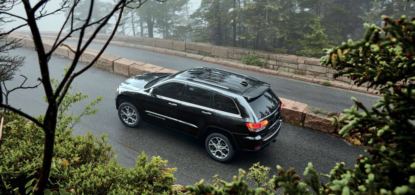 Display A view from above of the 2022 Jeep Grand Cherokee WK Limited being driven on a tree-lined street bordered by a brick wall.
