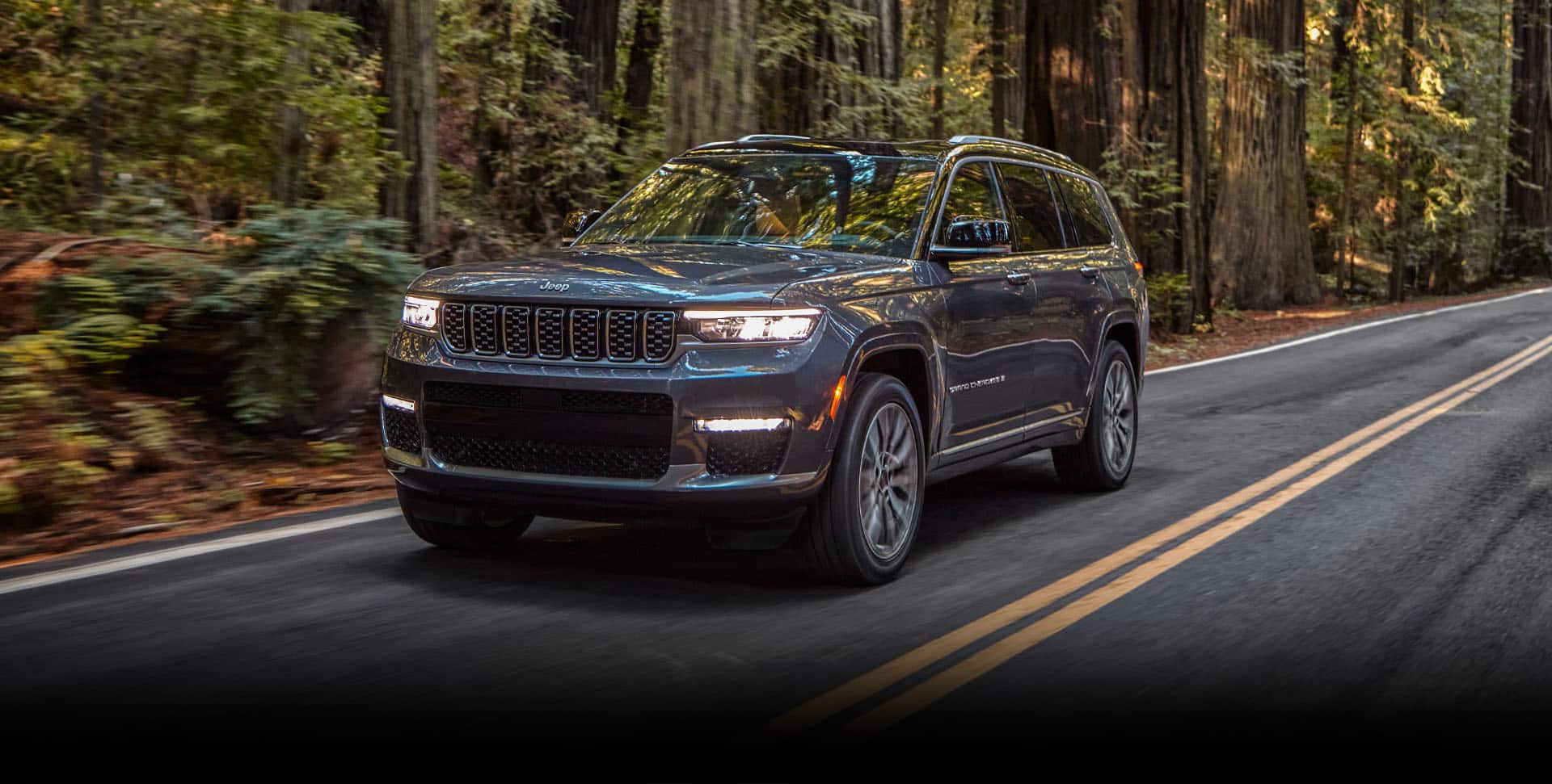 The 2022 Jeep Grand Cherokee L Summit being driven on a paved road surrounded by trees.
