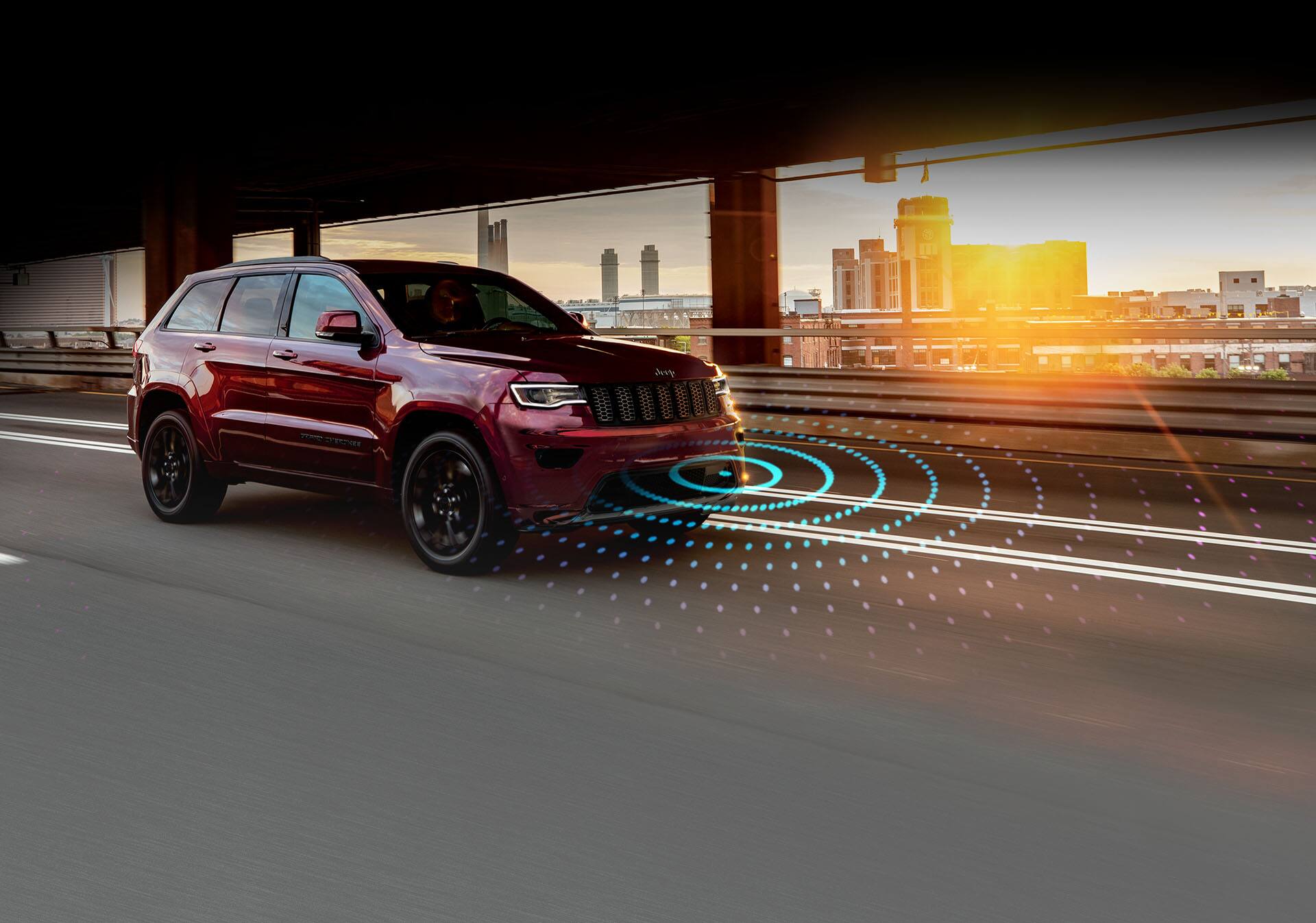The 2022 Jeep Grand Cherokee WK Laredo X with the Altitude Appearance Package and illustrated sensor bars emanating from its front end as it's driven on an empty road.