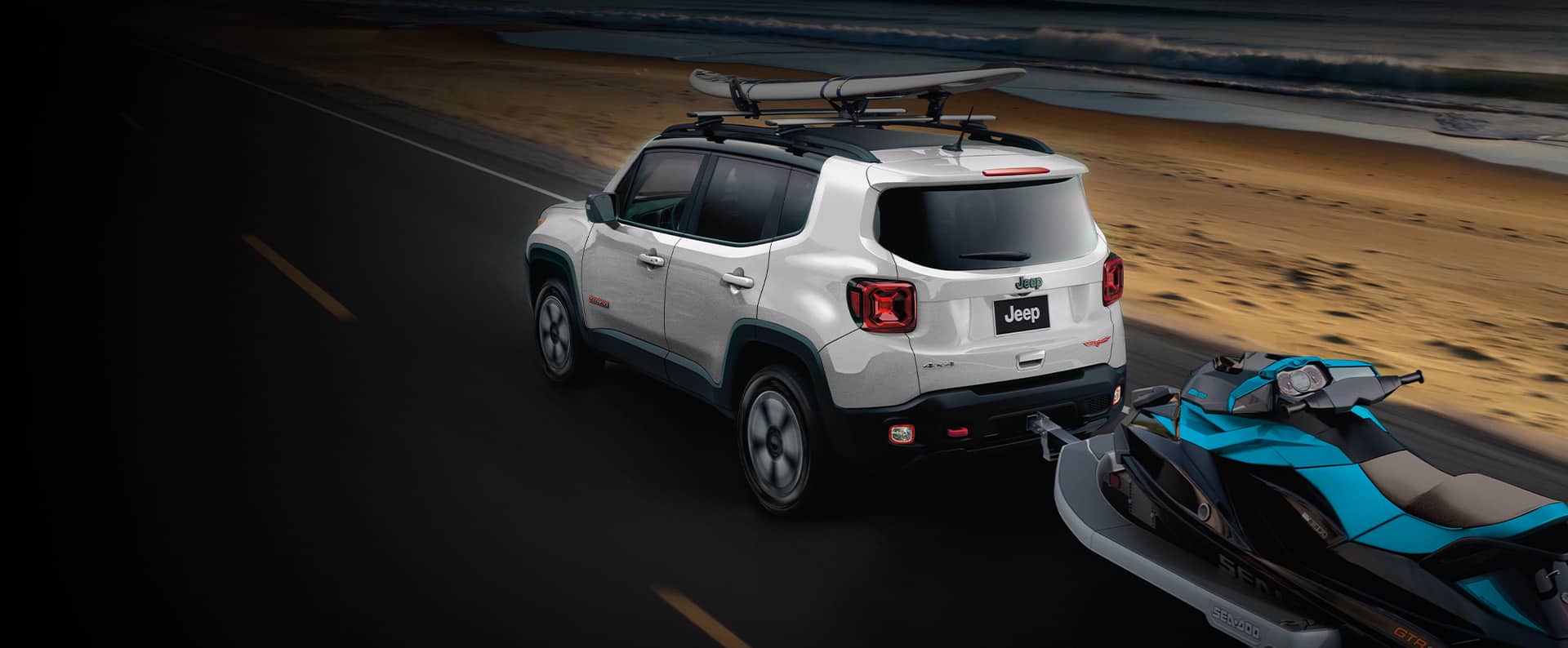 The 2022 Jeep Renegade towing a personal watercraft on a trailer while carrying a surfboard on its roof rack.