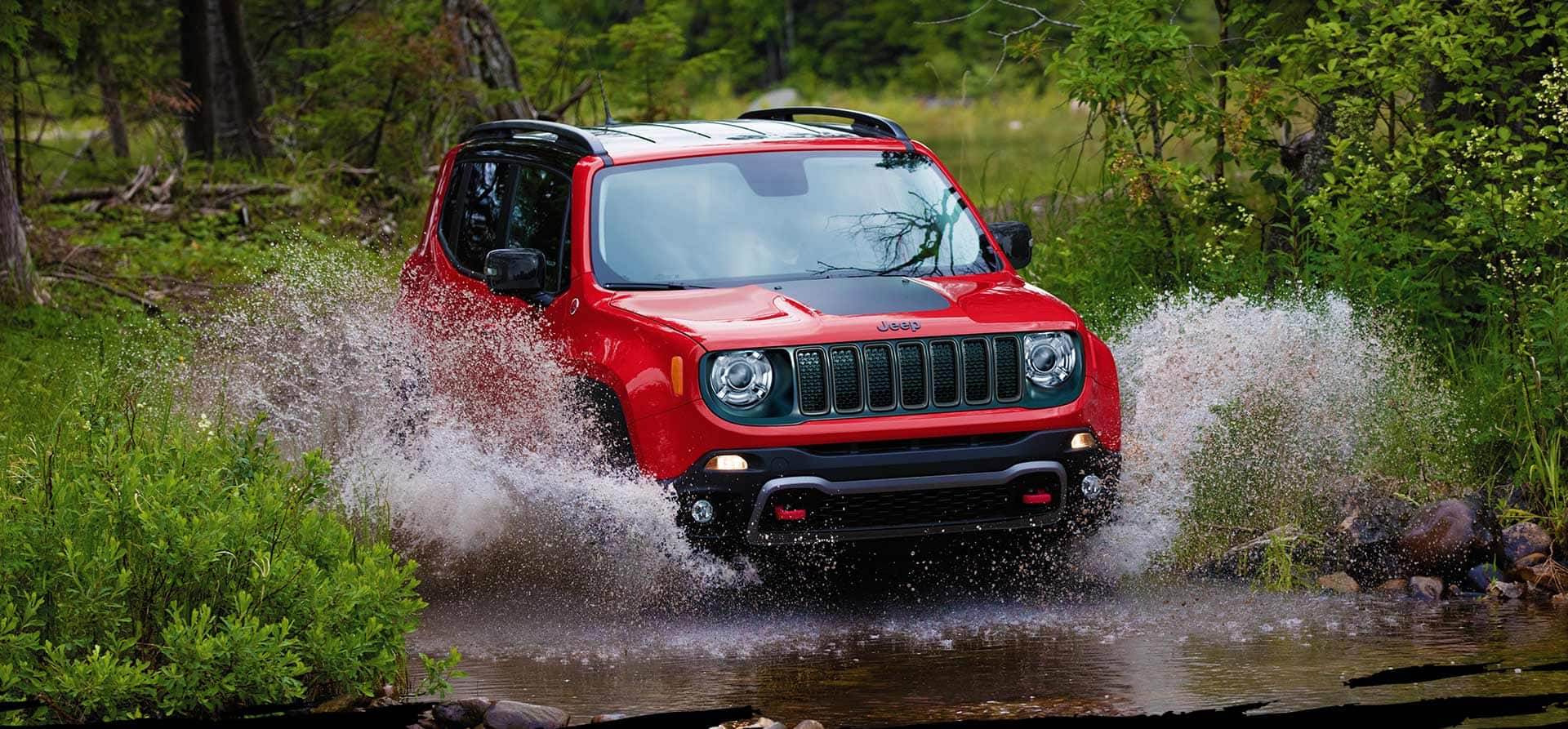 The 2022 Jeep Renegade Trailhawk being driven through a stream, water splashing up over its wheel wells.