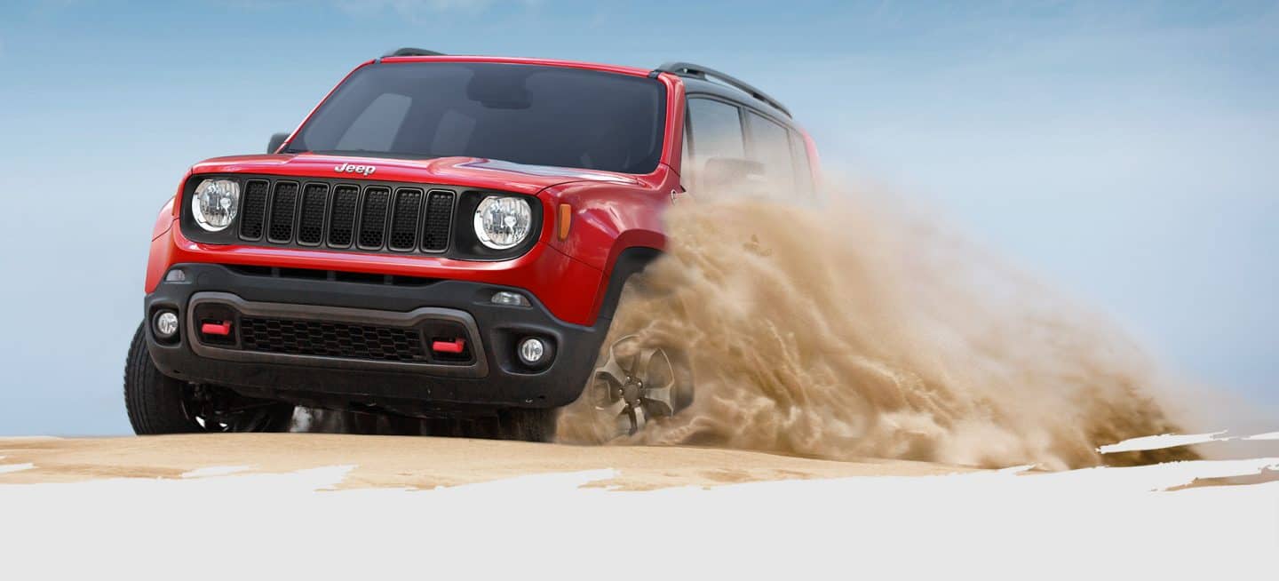 The 2022 Jeep Renegade Trailhawk being driven off-road in sandy terrain, with a large dust cloud obscuring its wheels.