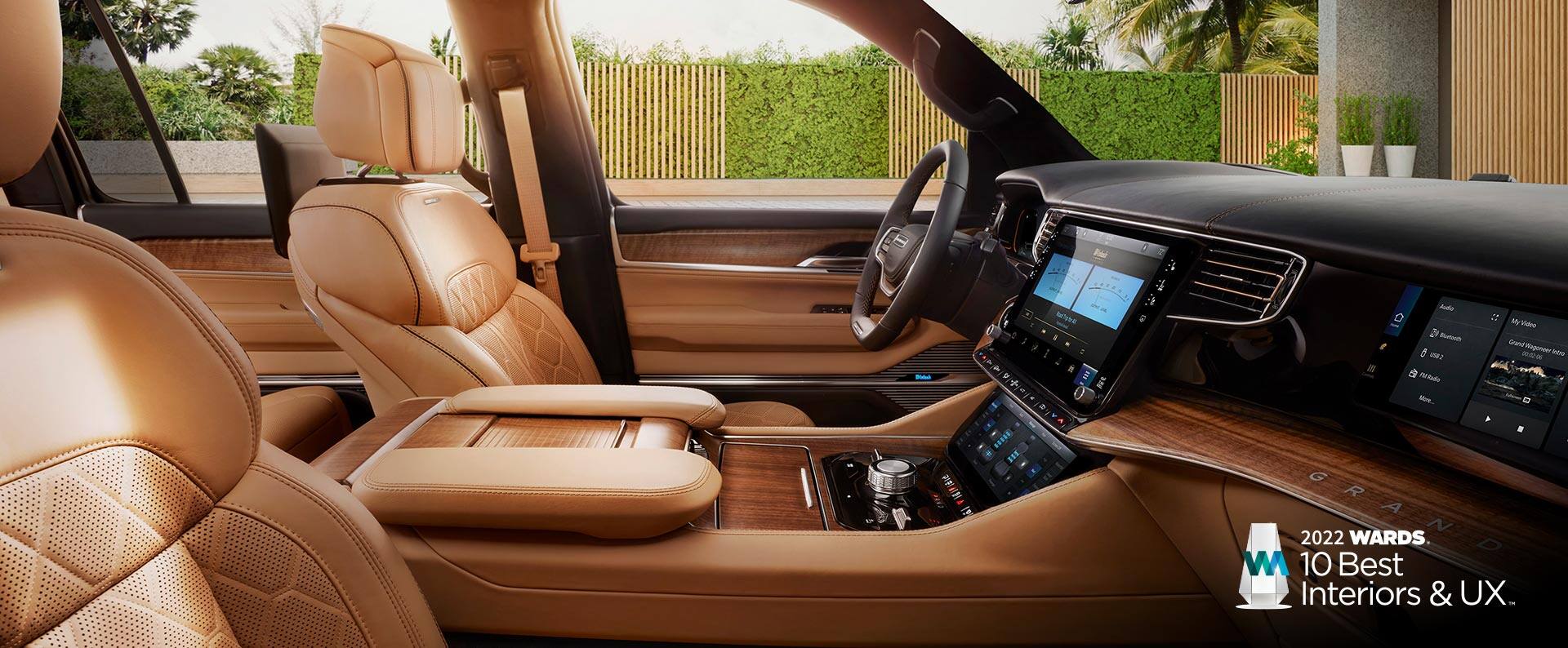 The front seats, steering wheel, center stack controls and driver and front passenger touchscreens in the 2022 Grand Wagoneer Series III. The 2022 Wards 10 best interiors and UX award logo.