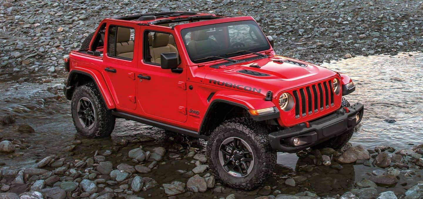 Display The 2022 Jeep Wrangler Rubicon parked on a rocky shore right at the water's edge.