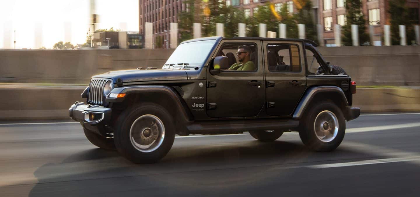 Display The 2022 Jeep Wrangler Sahara being driven on a city street.