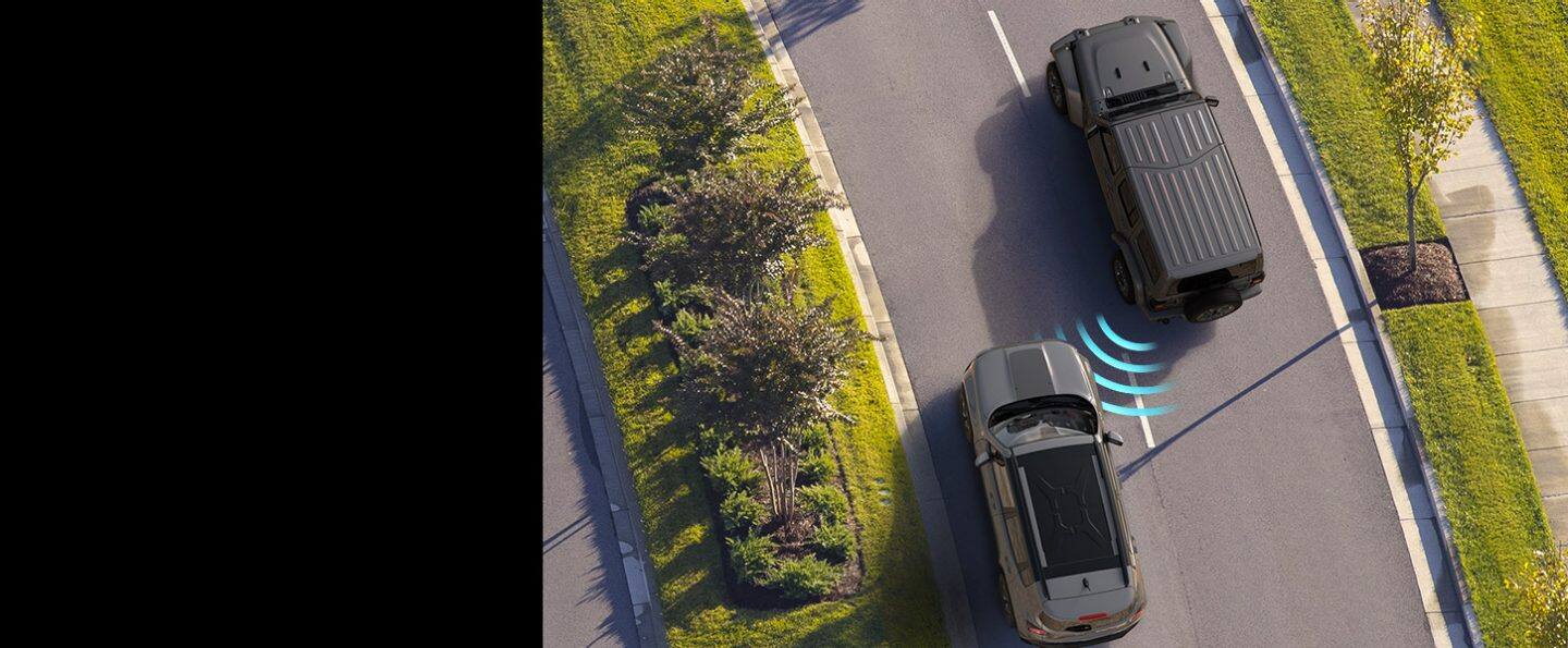 El Jeep Wrangler Sahara 2022 con barras de sensores ilustradas que emanan de la parte de atrás del vehículo, cruzándose con un vehículo que se aproxima por el carril contiguo.