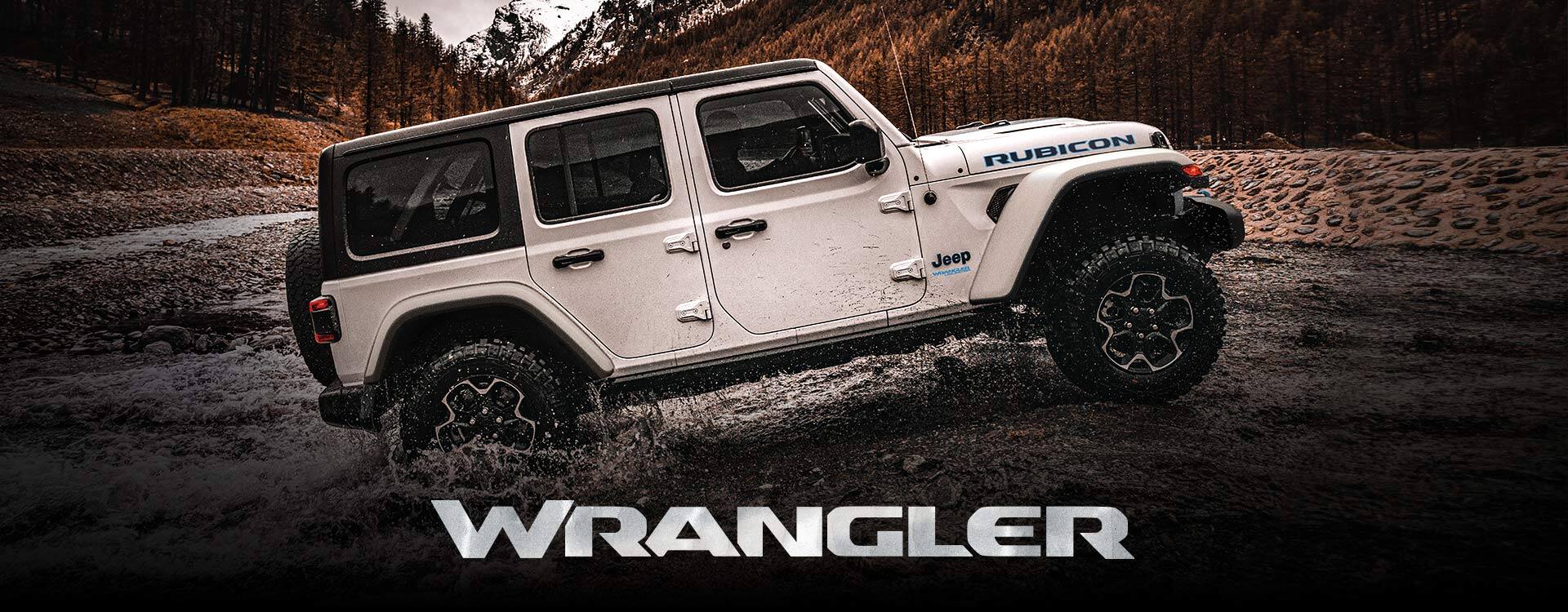 A profile view of a white 2022 Jeep Wrangler Rubicon 4xe pulling out of a stream, with forests and mountains in the background. Wrangler.
