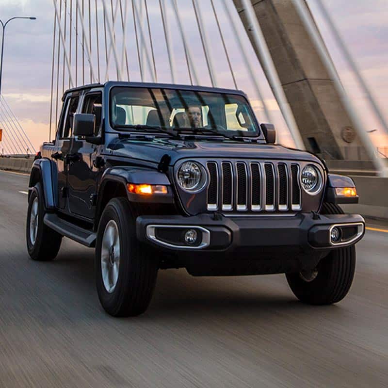 A front view of a 2022 Jeep Wrangler Sahara being driven on a suspension bridge.